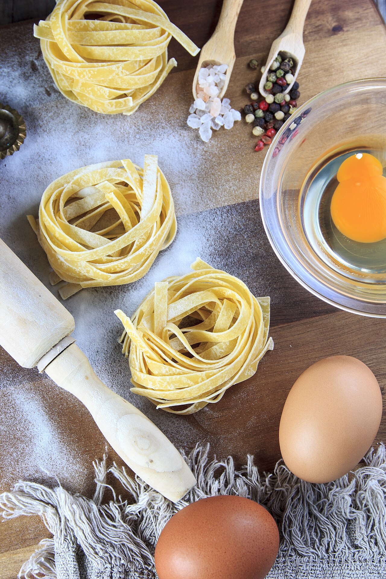 Nidi di tagliatelle fresche con uova e farina sul tavolo di legno